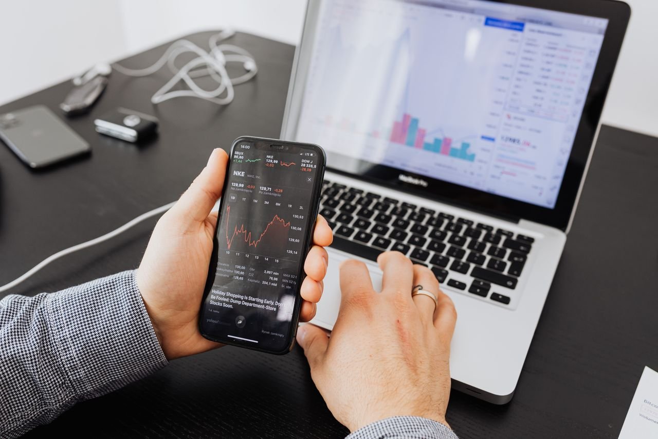 About Person analyzes stock data with a smartphone and laptop, indoors.